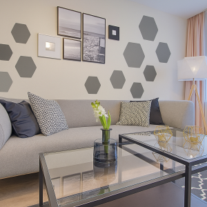 Pared del salón decorada con plantillas de pared hexagonales grises, con un moderno sofá gris y una mesa de café de cristal.