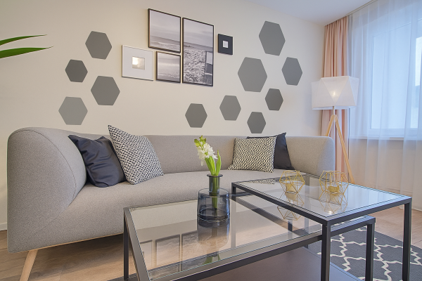 Pared del salón decorada con plantillas de pared hexagonales grises, con un moderno sofá gris y una mesa de café de cristal.