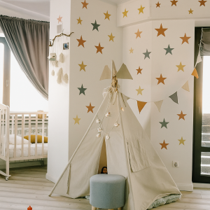 Colorful star wall stencil in a cozy kids room with a beige play tent and wooden flooring
